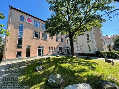 a building with a tree in front of a yard at 1, 2, sleep Boardinghouse Unterschleißheim Zentrum in Unterschleißheim