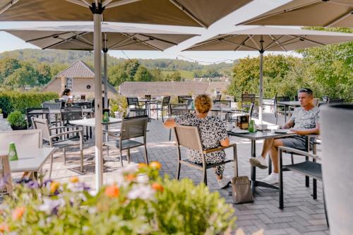 two people sitting at tables under umbrellas on a patio at B&B Brasserie Villare in Wijlre