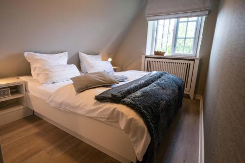 a bedroom with a bed with white sheets and a window at Smuk Huus in Nieblum