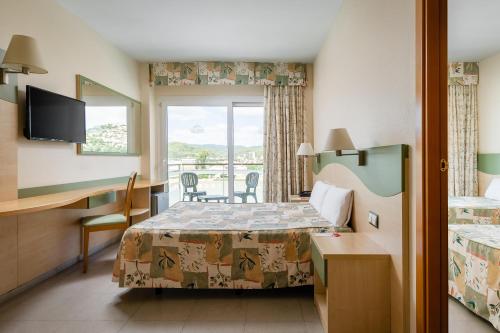 a hotel room with a bed and a desk and a window at ALEGRIA Caprici Verd in Santa Susanna