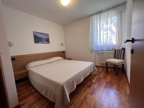 ein Schlafzimmer mit einem Bett, einem Fenster und einem Stuhl in der Unterkunft 078 Trilocale Baldino, Pinzolo in Pinzolo