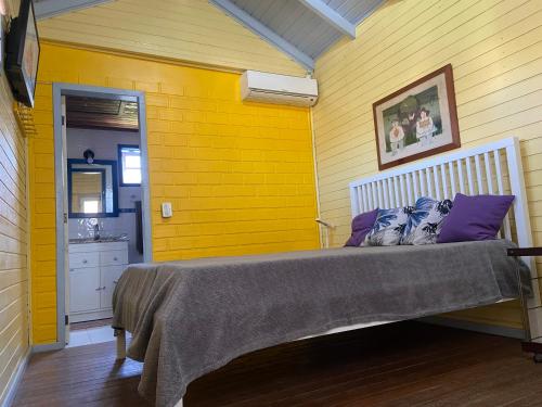 1 dormitorio con pared amarilla y cama con almohadas moradas en Casa Guarda do Embaú, en Guarda do Embaú