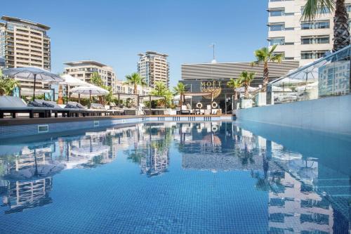 a large swimming pool with palm trees and buildings at Hilton Diagonal Mar Barcelona in Barcelona