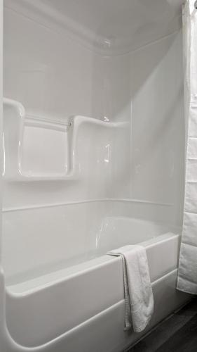 a white bathroom with a bath tub with a towel at Knights Inn Bracebridge in Bracebridge