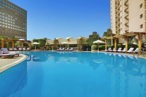 ein großer blauer Pool mit Stühlen und Sonnenschirmen in der Unterkunft Conrad Cairo Hotel & Casino in Kairo