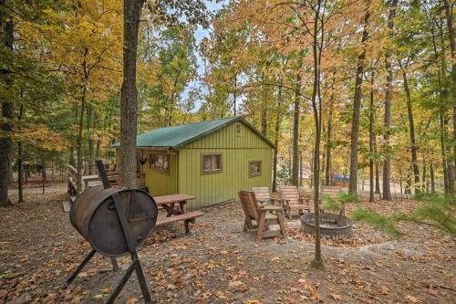 a green cabin in the woods with a grill and picnic tables at 5 Mi to Raystown Lake Launch Lucas McCain Cabin in Huntingdon