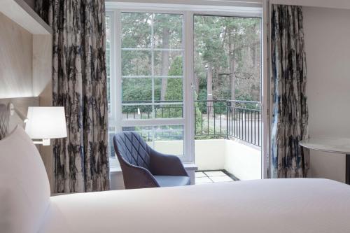 a bedroom with a bed and a chair and a window at Hilton Cobham in Cobham