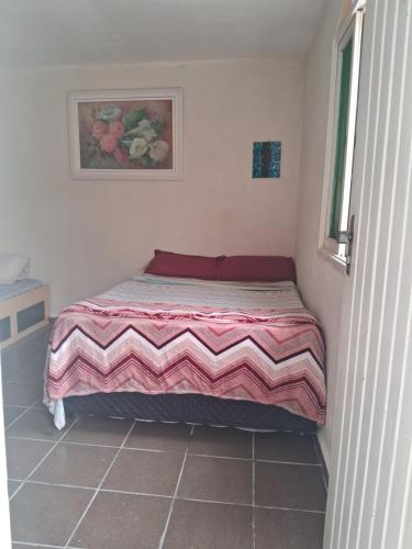 Cama en habitación pequeña con manta rosa y blanca en Loft Praia do Sonho, en Itanhaém