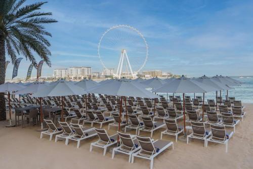 un mucchio di sedie e ombrelloni su una spiaggia di Hilton Dubai The Walk a Dubai