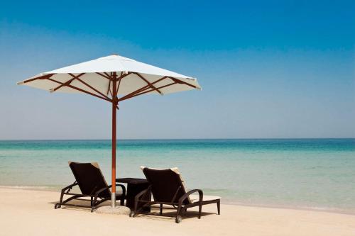 two chairs and a table under an umbrella on the beach at Hilton Dubai Jumeirah in Dubai