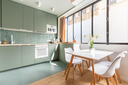une cuisine avec des placards verts ainsi qu'une table et des chaises blanches dans l'établissement Rome Batignolles - Luxe Charme - 2P, à Paris
