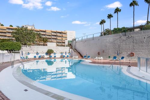 Una piscina en un resort con sillas y palmeras. en Holiday Home Luxury Loft GC, en Maspalomas
