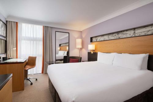Habitación de hotel con cama blanca grande y escritorio. en Hilton London Kensington Hotel en Londres