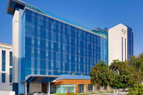 a large glass building in front of two tall buildings at Aloft Al Mina, Dubai Jumeirah in Dubai