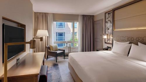 um quarto de hotel com uma cama, uma secretária e uma televisão em Hilton Munich City em Munique