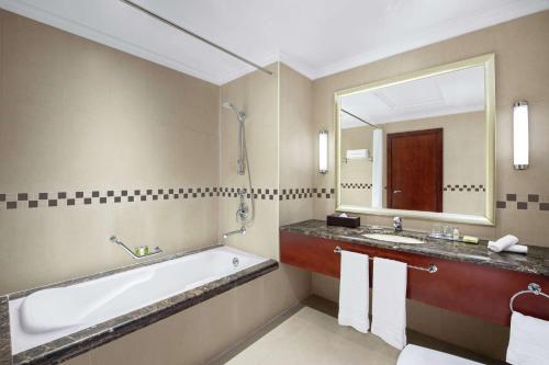 a bathroom with a tub and a sink and a mirror at DoubleTree by Hilton Ras Al Khaimah in Ras al Khaimah