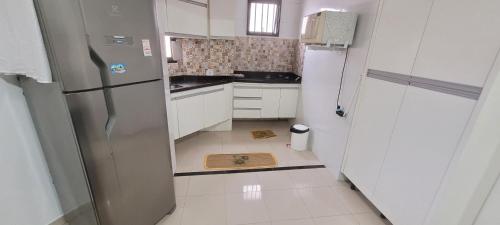 una pequeña cocina con armarios blancos y nevera. en Guarujá enseada sp, en Guarujá