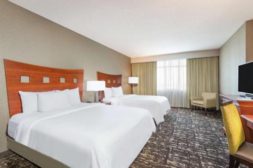 a hotel room with two beds and a flat screen tv at Embassy Suites by Hilton Saint Louis Saint Charles in St. Charles