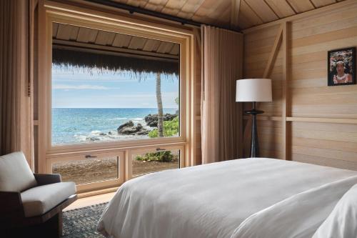 a bedroom with a large window overlooking the ocean at Kona Village A Rosewood Resort in Kailua-Kona