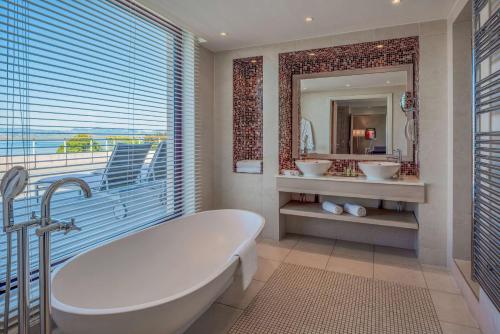La salle de bains est pourvue d'une baignoire, de 2 lavabos et d'un miroir. dans l'établissement Hilton Evian Les Bains, à Évian-les-Bains