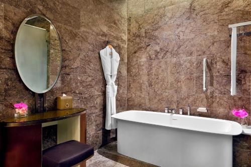 uma casa de banho com uma banheira e um espelho. em AlRayyan Hotel Doha, Curio Collection by Hilton em Doha