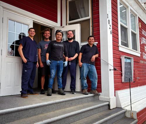 a group of men standing outside of a red house at The Downtown, a Coast Hotel in Dawson City