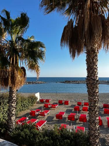 einen Strand mit roten Stühlen, Palmen und dem Meer in der Unterkunft Casa indipendente vista mare in Imperia