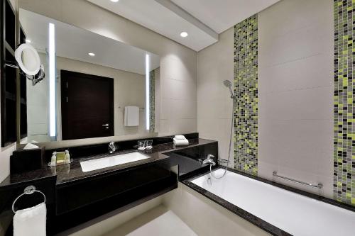 a bathroom with a tub and a sink and a mirror at Doubletree By Hilton Doha - Al Sadd in Doha