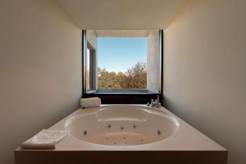 Boeira Garden Hotel Porto Gaia, Curio Collection by Hilton في فيلا نوفا دي غايا: حوض استحمام كبير في غرفة مع نافذة