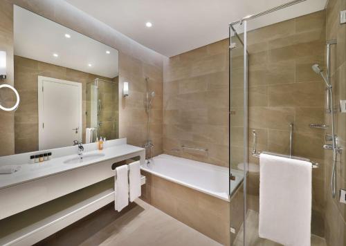 a bathroom with a tub and a sink and a shower at Aleph Doha Residences, Curio Collection By Hilton in Doha