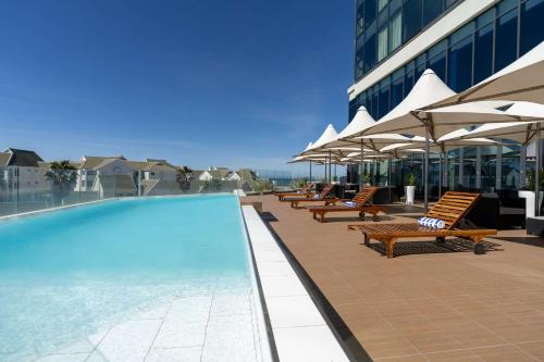 ein Pool auf dem Dach eines Gebäudes mit Stühlen und Sonnenschirmen in der Unterkunft Radisson Blu Hotel, Port Elizabeth in Port Elizabeth