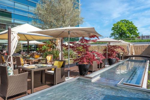 a swimming pool with tables and umbrellas next to a pool at Hilton Geneva Hotel and Conference Centre in Geneva