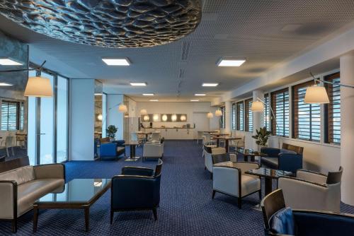a waiting room with chairs and tables and windows at Hilton Geneva Hotel and Conference Centre in Geneva