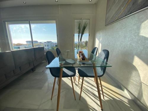 luxury condo with sea view في طنجة: غرفة طعام مع طاولة زجاجية وكراسي زرقاء