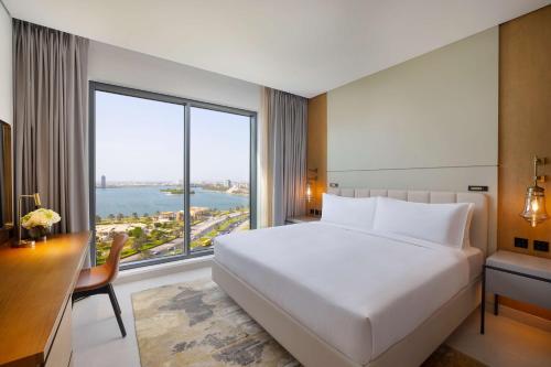 a bedroom with a bed and a desk and a large window at DoubleTree by Hilton Sharjah Waterfront Hotel And Residences in Sharjah