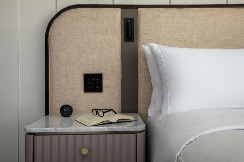 a bed with a side table with a book and glasses at Conrad Nashville in Nashville