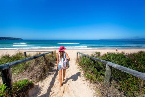 a woman walking down a path to the beach at Tween Waters Merimbula in Merimbula