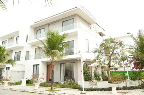 a white building with palm trees in front of it at Sea Villa - FLC Sam Son in Sầm Sơn