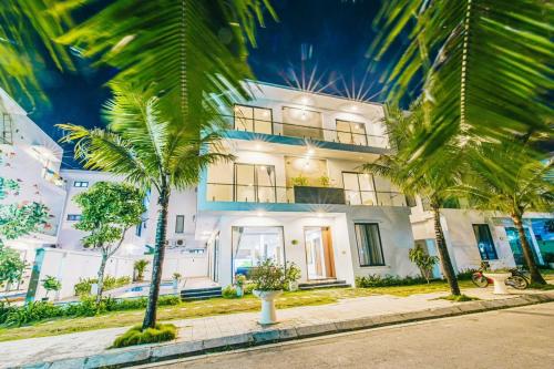 a large white house with palm trees in front of it at Sea Villa - FLC Sam Son in Sầm Sơn