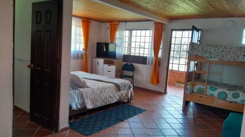 1 dormitorio con 1 cama, TV y ventanas en Quinta Los Llanitos Hospedaje Campestre, en Guatavita