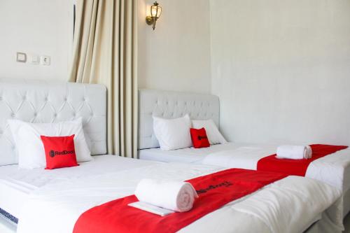 two white beds with red pillows in a room at RedDoorz Syariah near Kawasan Wisata Gunung Prau Dieng in Dieng
