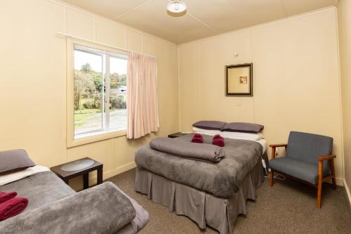 een kamer met 3 bedden, een stoel en een raam bij Kaniere Hotel in Hokitika