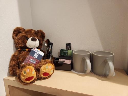 a teddy bear sitting on a shelf next to two mugs at Travelodge Honmachi Osaka in Osaka