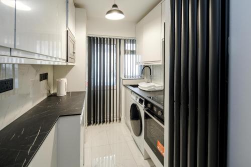 cocina con armarios blancos, lavadora y secadora en CommonSide Luxury en Mitcham