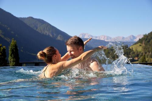 un hombre y una mujer jugando en el agua en Hotel Quelle Nature Spa Resort en Santa Maddalena in Casies