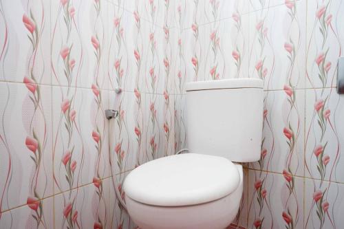 a white toilet in a bathroom with flowers on the wall at RedDoorz near Alun Alun Wonosobo 2 in Wonosobo