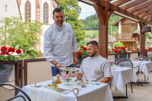 een chef die naast een man aan een tafel staat bij Hotel-Gasthaus Goldener Engel in Glottertal