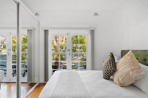a white bedroom with a bed and a balcony at The Young - A Peaceful Parkside Delight in Sydney