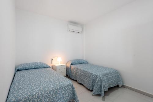two beds in a white room with blue comforter at Casa Mar de frente in Málaga