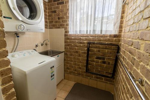 a small bathroom with a washing machine and a brick wall at Beachfront Apartments in Merimbula